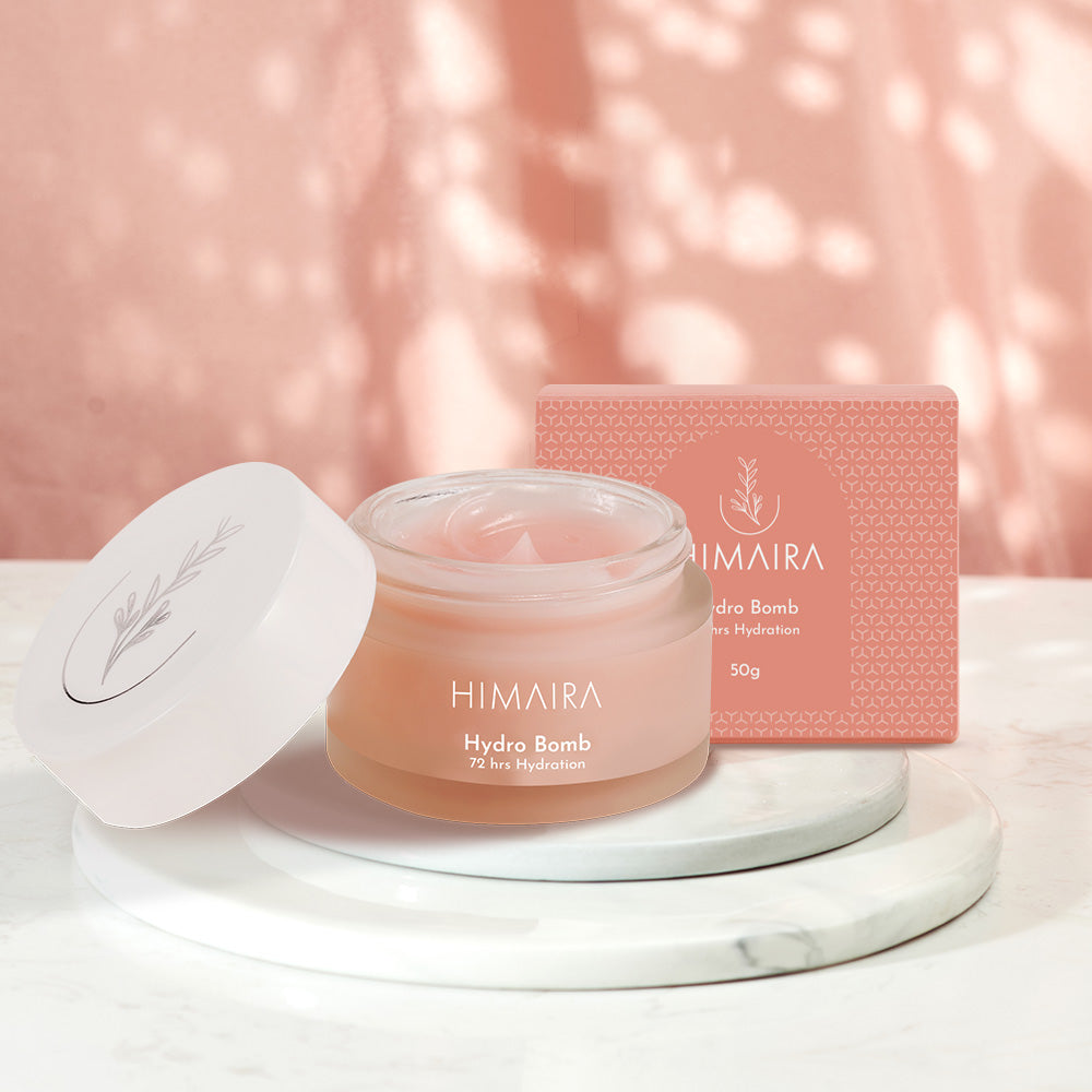 A jar of Hydro Bomb Moisturizer by Himaira placed with its packaging box, displayed on a marble surface with a soft pink background.