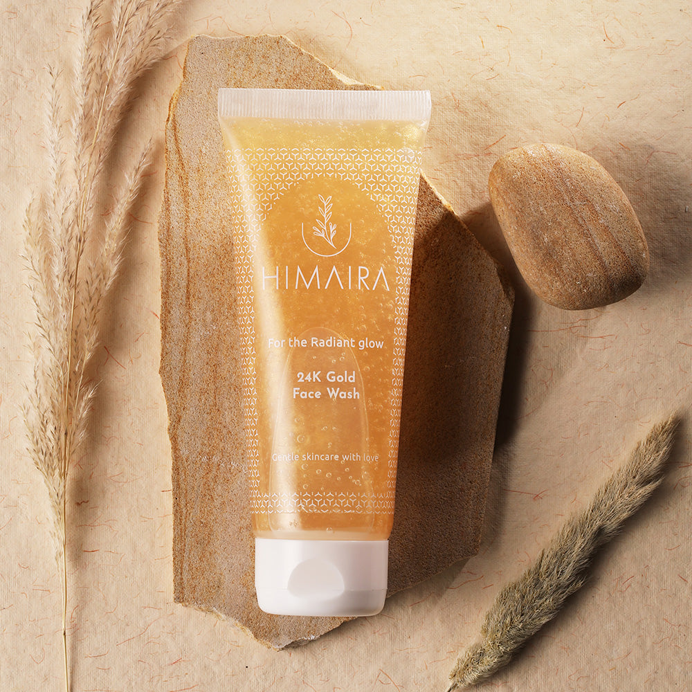 Product shot of a tube of Himaira 24K Gold Face Wash, a gentle skincare product for a radiant glow, against a textured, earthy background.
