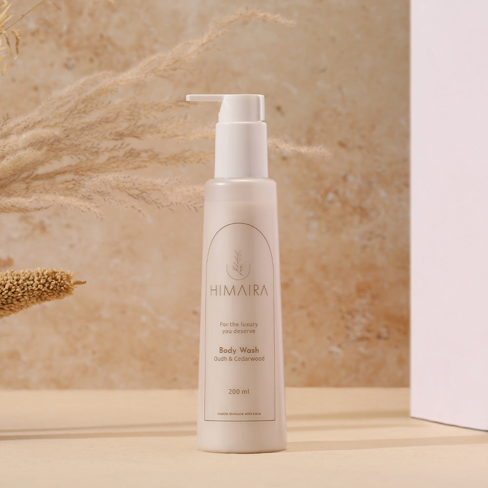 Himaira Body Wash Oudh & Cedarwood, 200 ml pump bottle standing on a beige stone surface with dried grasses and warm studio light.