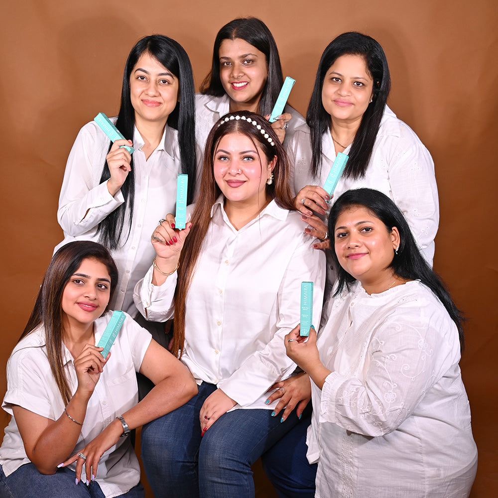 A group of six women, all wearing white shirts, pose together while holding up a tube of Himaira&