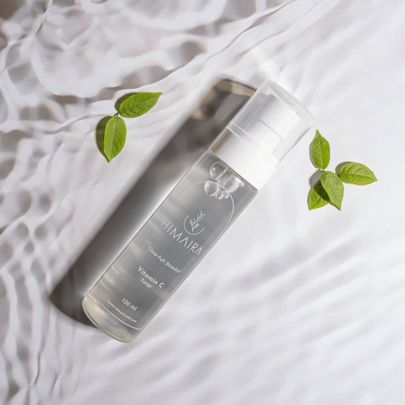 Close-up product shot of Best Vitamin C Toner in a clear 100 ml bottle, soft reflections on white with small green leaves
